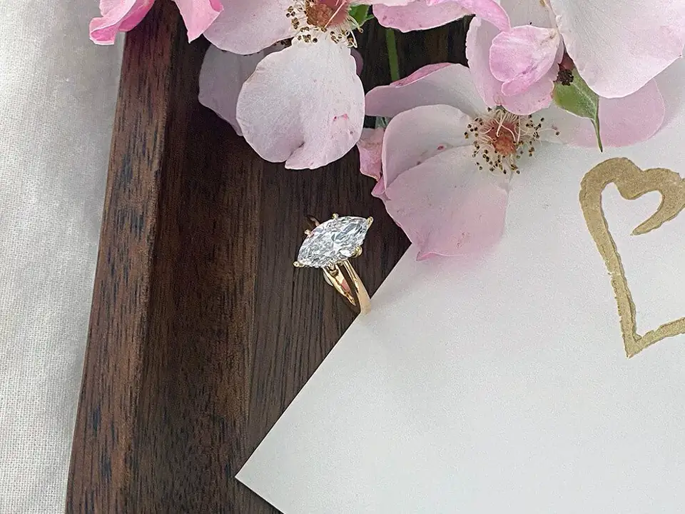 Gold engagement ring with a marquise diamond beside blossoms
